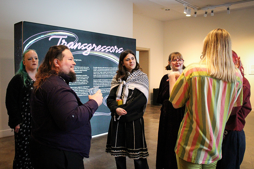 Six people standing together inconversation in front of a sign that says Transgressors.