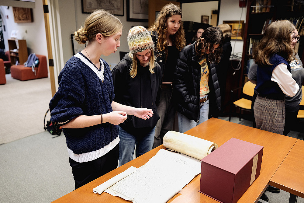 A group of 5 people gathered around a table of items from an archive collection.