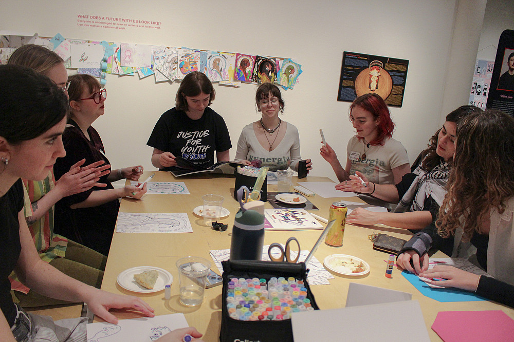 Eight students seated around a table with art supplies.