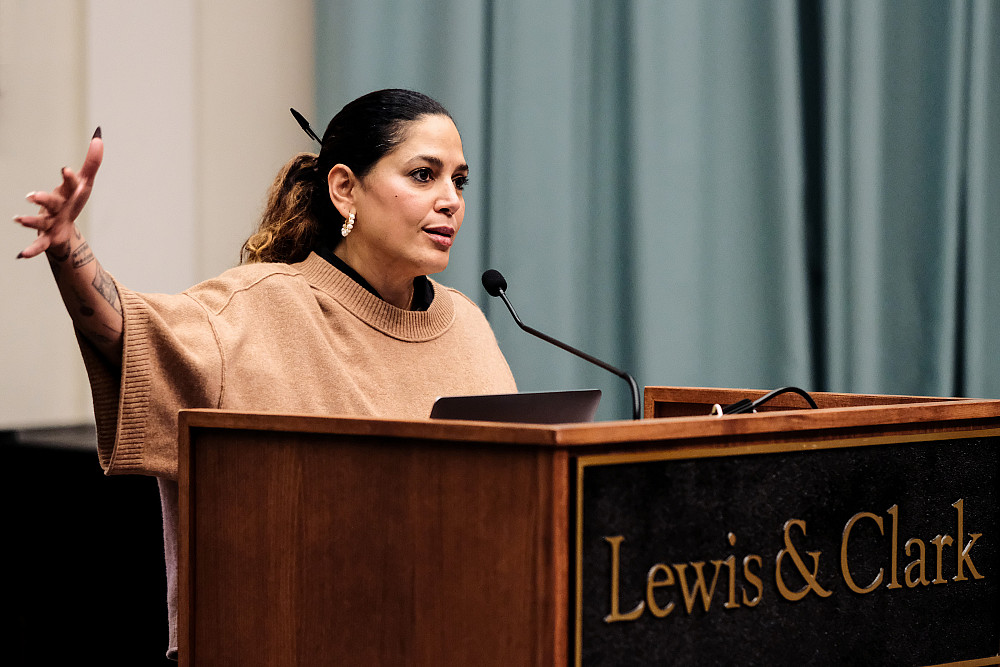 Close up of keynote speaker raising their right hand as they speak behind a Lewis & Clark podium