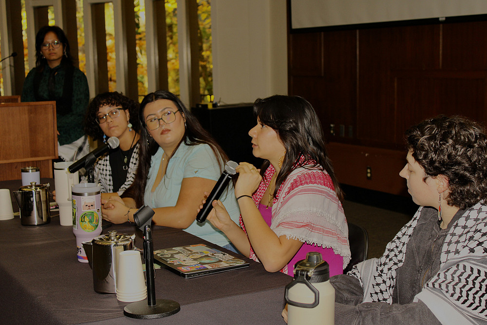 Students sitting at a table in the Council Chambers, one holding a microphone answering a question about their research.