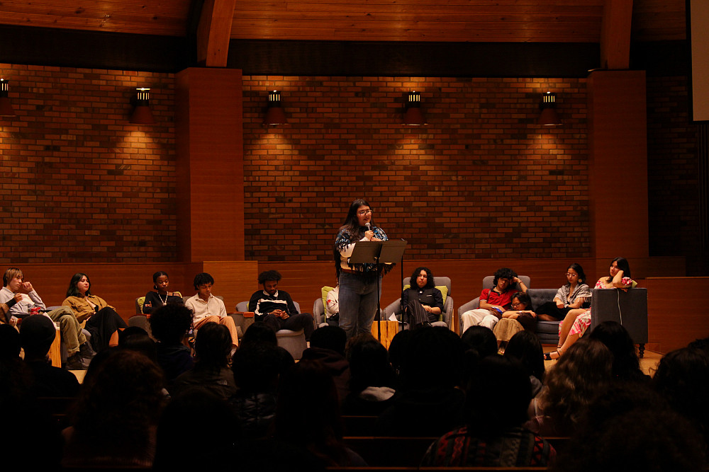 The audience at Race Monologues listening to a student standing on stage in the Agnes Flanagan Chapel, speaking into a microphone