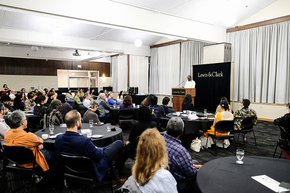 Individuals sitting at dinner tables listening to a speech being given by a person at the podium