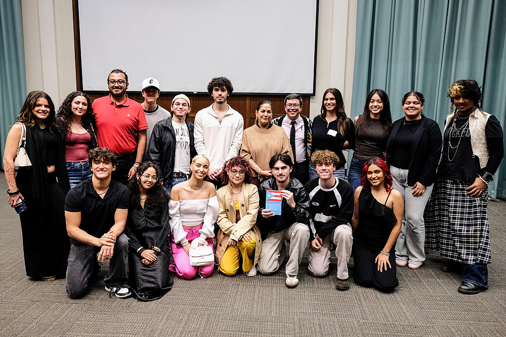 A group of students with the keynote presenters in the council chambers, one holding a book by Jorell Meléndez-Badillo