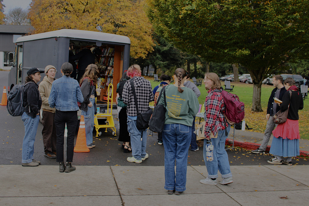 Students stand outside of a bus with books inside
