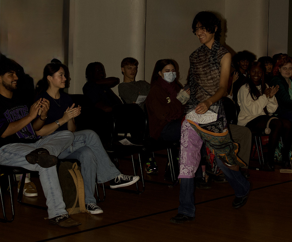 A student walks down the runway while audience members sit nearby, clapping