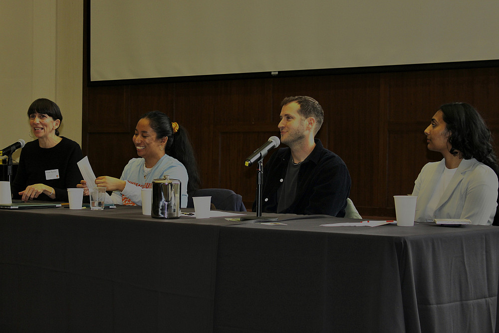 Three panelists and the panel moderator sit at a table in the council chambers, the moderator speaking into a microphone