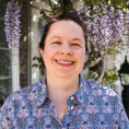 Photo of Melanie smiling in front of flowers