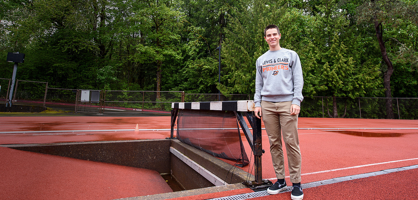 Joseph posing outside near a hurdle on the track.