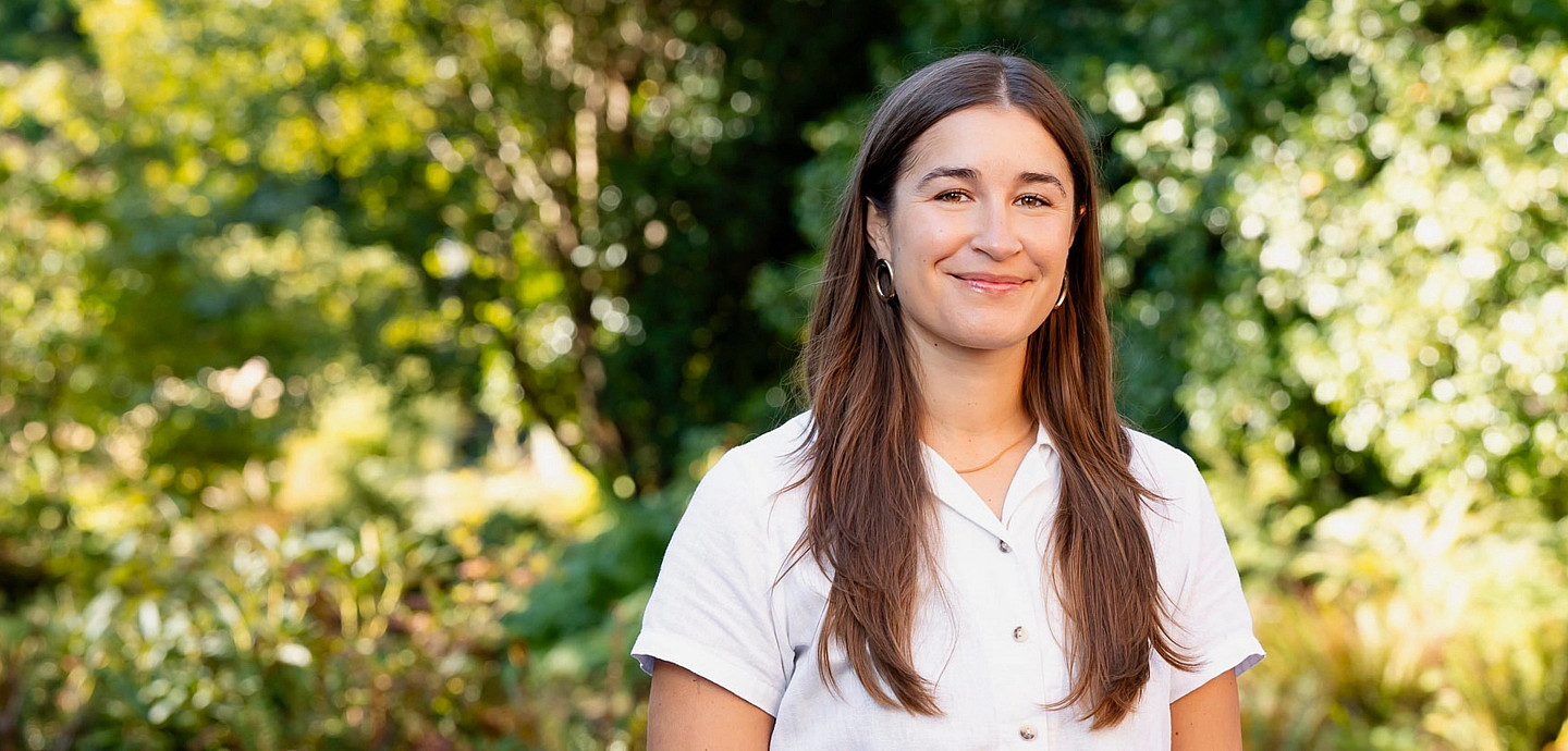 Hannah posing outside, wearing a white short-sleeve top.