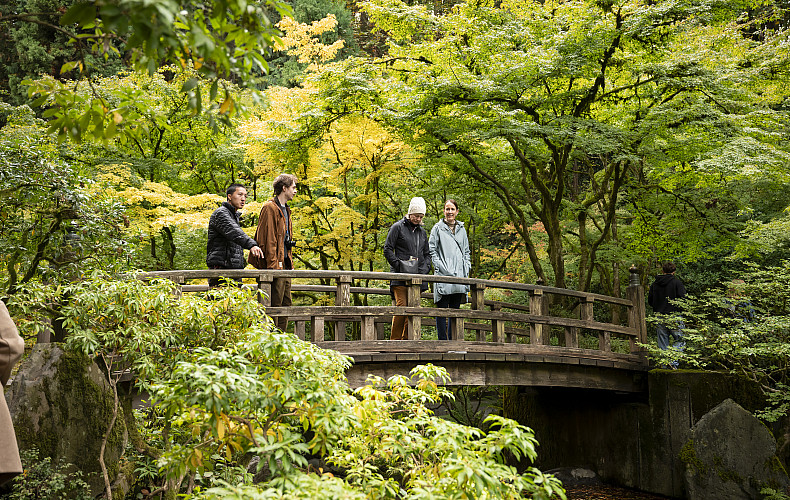 Four people standing on a bridge surrounded by greenery at the Portland Japanese Gardens.