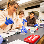 Students using science equipment and wearing blue gloves.