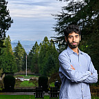 Ishan posing outside wearing a blue shirt, surrounded by green trees.