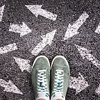 Sneaker shoes and arrows pointing in different directions on asphalt ground, choice concept