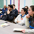 Students sitting together at a table, smiling at the teacher.