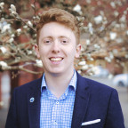 Rory posing outside wearing a blue shirt and navy suit jacket.