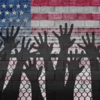 Shadow of hands reaching up over a chain link fence with an American flag as the background.