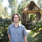 Cooper posing outside near a gazebo, wearing a blue button-up short sleeve shirt and glasses.
