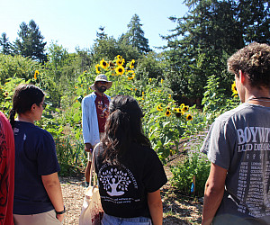 Students standing outside on a farm, listening to a man talk.