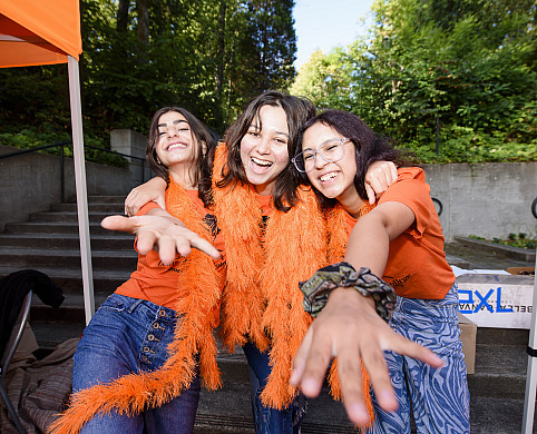 Three students smiling and reaching their hands out toward the camera.