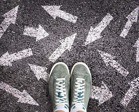 Sneaker shoes and arrows pointing in different directions on asphalt ground, choice concept