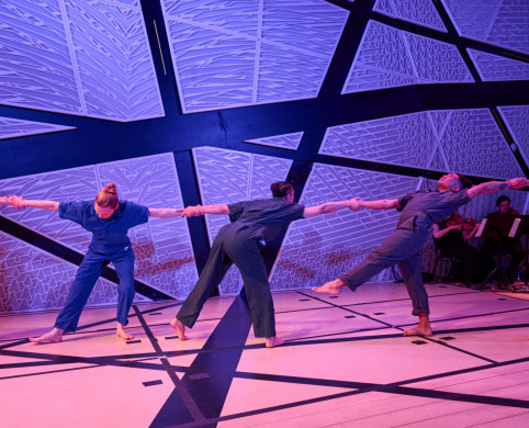 A line of dancers on stage holding hands in front of a colorful background.