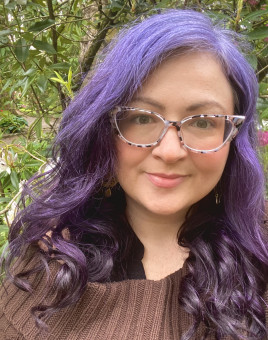 JaDee is smiling at the camera with trees and plants in the background 